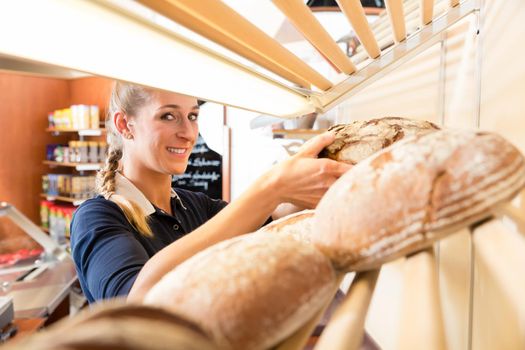 Bakery woman putting bread in shop shelf to sell it