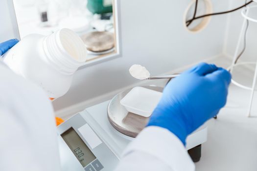 Closeup of pharmacist hand holding bottle while weighing white powder chemical in a laboratory