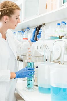 Young female doctor testing chemicals wearing labcoat and hand gloves in a laboratory