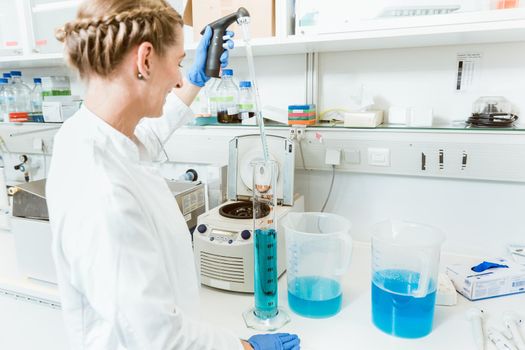 Young female doctor testing chemicals wearing labcoat and hand gloves in a laboratory
