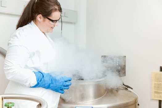 Young female doctor using sterilizing machine in laboratory wearing labcoat, gloves and eyeglasses for safety