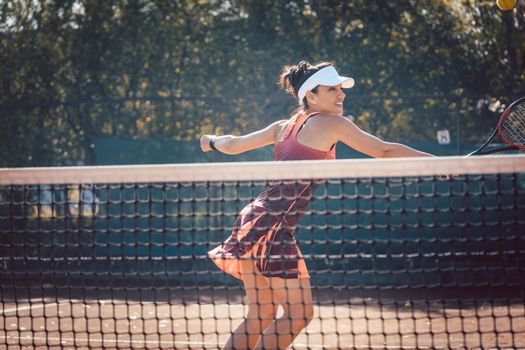 Woman in red sport dress playing tennis hitting the ball