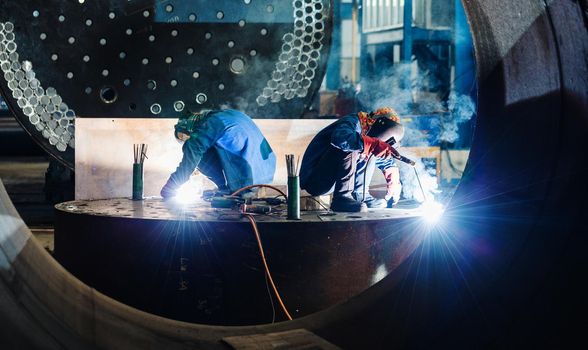 Two workers welding in the interior of a factory manufacturing metallic cylinders for industrial boilers