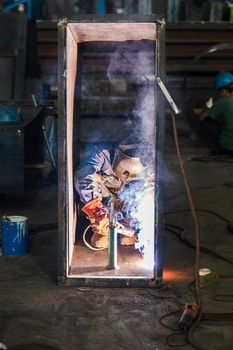 Blue-collar worker welding in the interior of a factory manufacturing industrial boilers