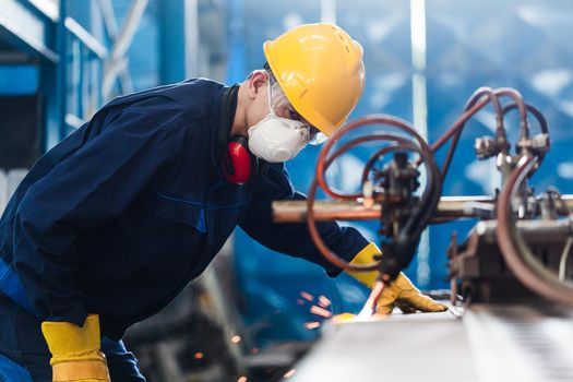 Asian worker wearing protective equipment while using CNC plasma cutter