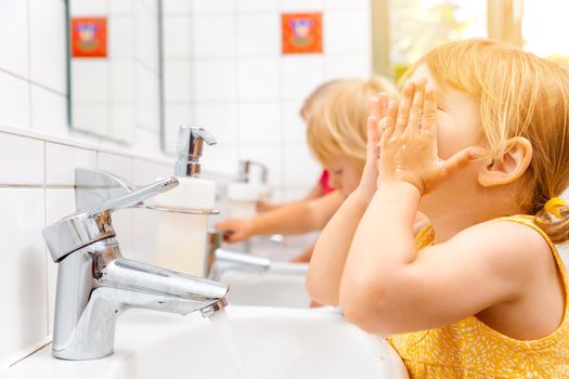 Child in kindergarten washing her hands in bathroom
