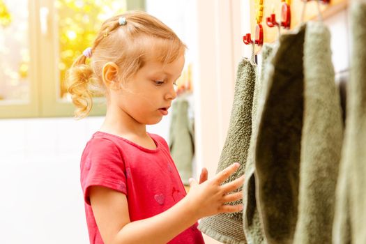 Little girl in nursery school using towel in bathroom drying her hands