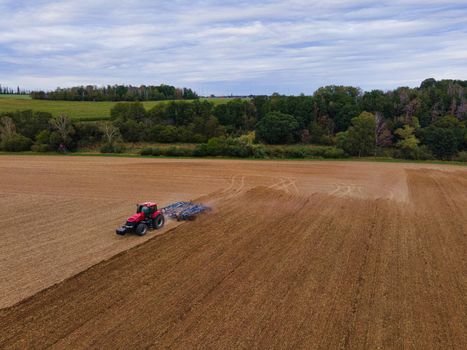 Farmer with tractor on wide field tilling the soil, aerial shot