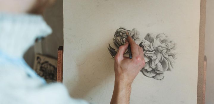 Close-up of man's hand drawing flower on easel