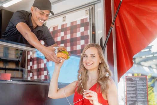 Beautiful woman getting a burger as takeout food from cook in food truck which makes her visibly happy