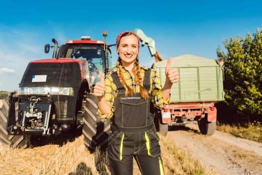 Farmer woman standing in front of agricultural machinery giving thumbs-up, ready for the harvest to start