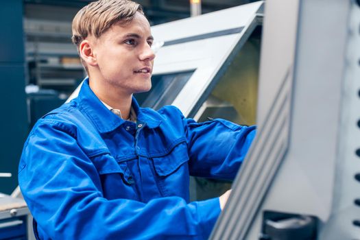 Young male worker programming lathe machine in factory