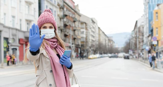 Woman wearing corona mask in city giving stop sign towards camera