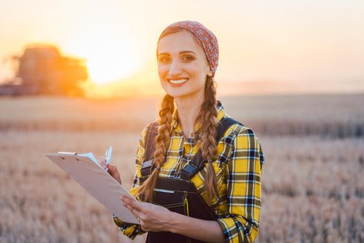 Farmer woman and combine harvester on wheat field during sunset