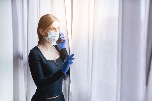 Woman in quarantine looking out of window using phone to call help for anxiety and depression