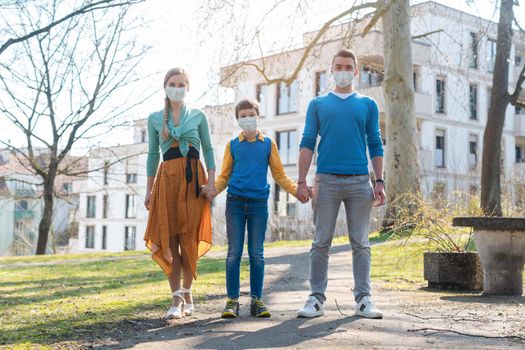 Family having a walk in the sun during corona virus emergency wearing face masks
