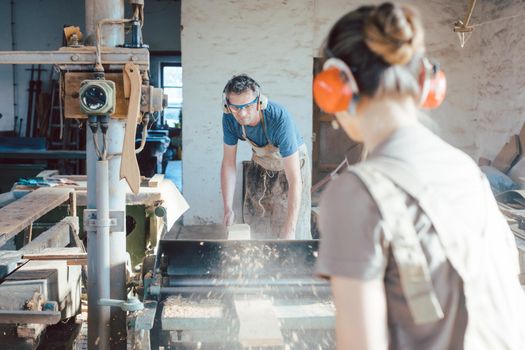 Team of carpenters planning wood using a machine, woman and man