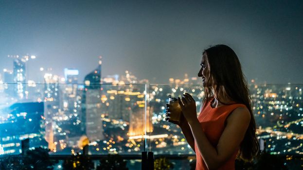 Woman having a drink on roof terrace overlooking the city skyline