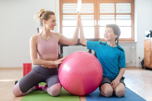 Mother and son giving each other a high-five after fitness exercise at home with pink ball