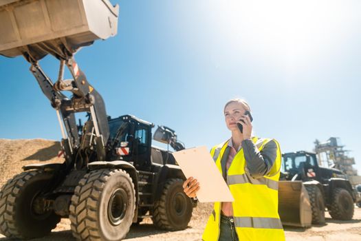 Worker woman with phone and clipboard in mine or quarry doing her job