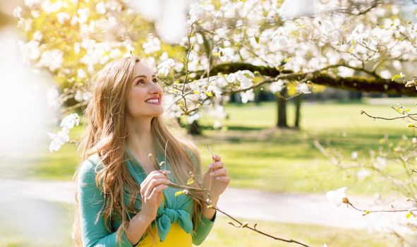 Beautiful woman enjoying the spring blossom in a park under a tree