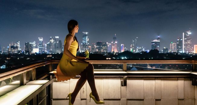 Woman having a drink on roof terrace overlooking the city skyline