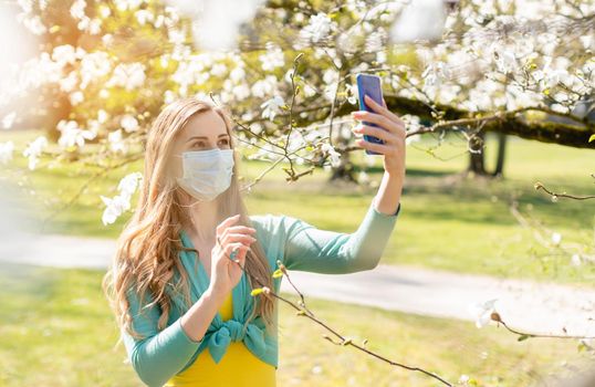 Woman taking a selfie with her phone in spring during Covid-19 crisis wearing a mask