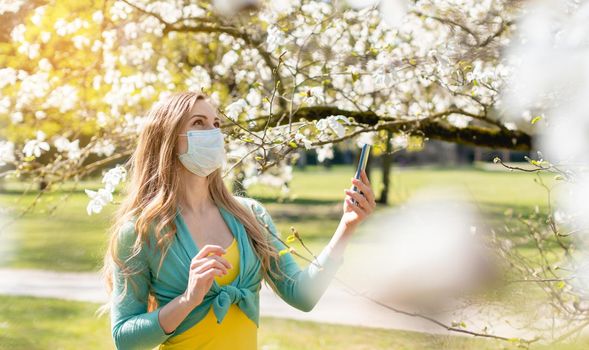 Woman enjoying the spring blossom despite the Coronavirus crisis taking picture with her phone