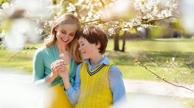 Son giving his mom flowers for mothers day under a blossoming tree in spring