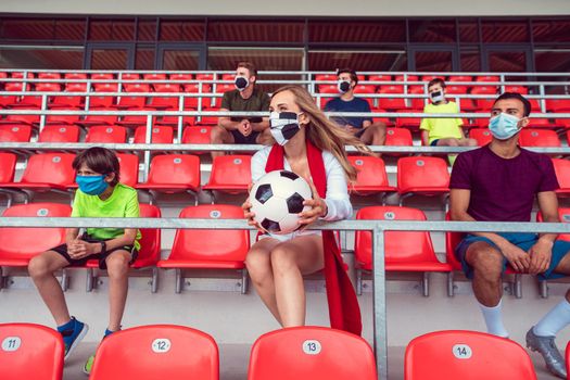 Fans with masks during covid-19 in soccer stadium keeping distance with lots of empty seats