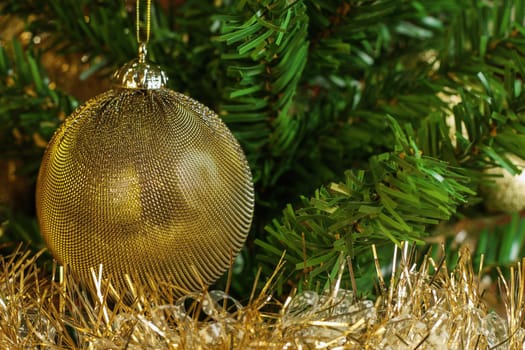 Horizontal image of the detail of golden decoration on the christmas tree with gold chain. Gold and green colours 