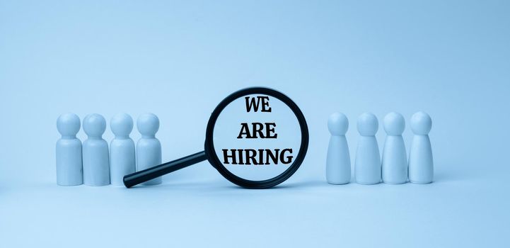 wooden figures of men stand on a blue background and a black magnifying glass. Recruitment concept, search for talented and capable employees, career growth