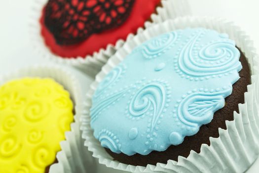 Three cupcakes on the white background. Yellow, blue and red with handmade decoration