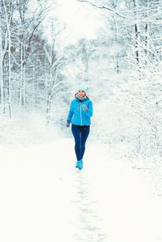 Woman jogging towards camera in cold and snowy forest for fitness gains