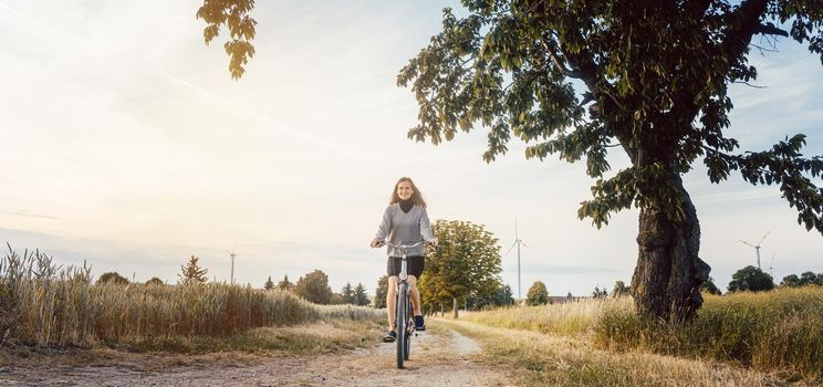 Woman on a bicycle having fun in rural landscape during sunset