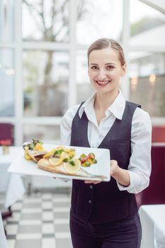 Waitress in a nice restaurant presenting a tasty dish to the camera