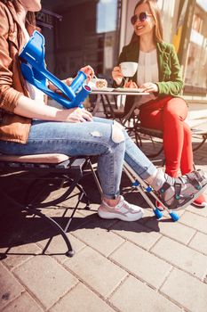 Two women, one with a broken leg and crutches, in a cafe having coffee and cake