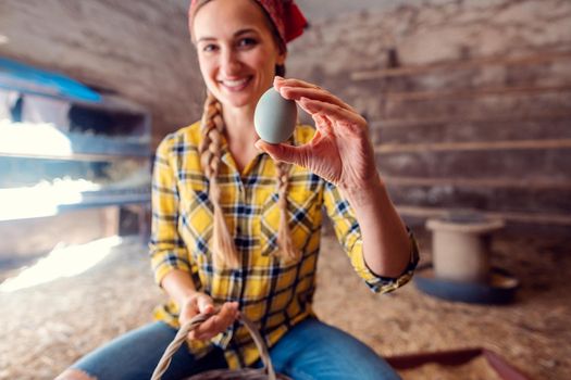 Happy farmer woman showing egg she just collected in a henhouse