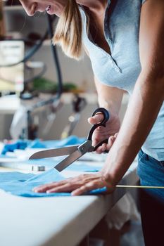 Woman cutting fabric with tailor scissors on tailor's table in a studio