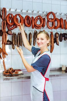 Woman actively recommending sausages in her butchery shop taking them from the hook