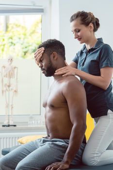 Woman physical therapist massaging young black man holding his head