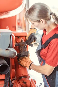 Woman machinist working with wrench of a farm machine doing some fixing or maintenance