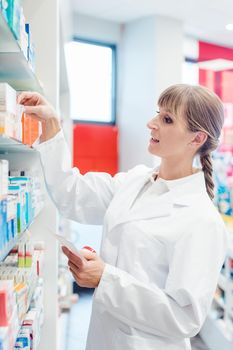Smiling pharmacist or Chemist woman sorting drugs in shelves in her pharmacy