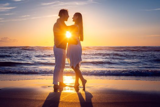 Romantic couple in love kissing on the beach during sunset, backlit scene