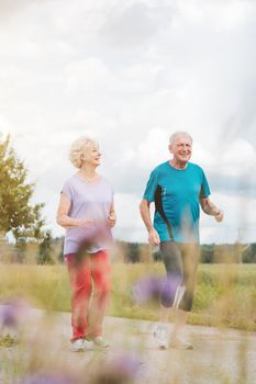Fit and active senior couple running outdoors as exercise on path in summer