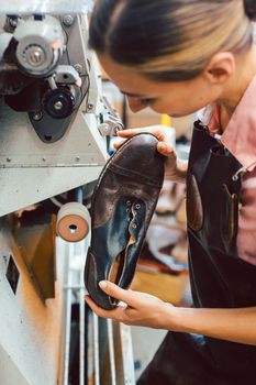 Woman cobbler working on machine in her shoemaker workshop adjusting the settings