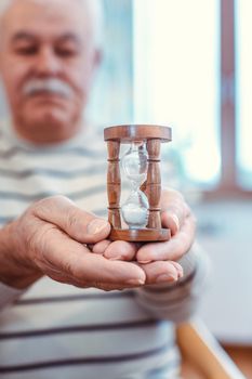 Senior man holding hourglass in retirement home, symbol for limited life span