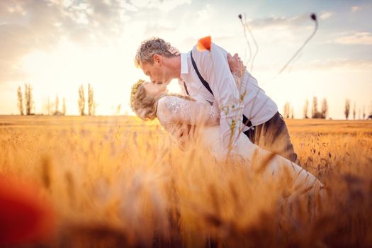 Wedding couple kissing in romantic setting on a wheat field during sunset