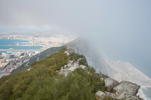 Aerial view of top of Gibraltar Rock, in Upper Rock Natural Reserve: on the left Gibraltar town and bay, La Linea town in Spain at the far end, Mediterranean Sea on the right in fog United Kingdom, Europe.