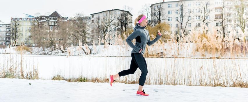 Woman running for sport in front of apartment buildings on winter day on snow path